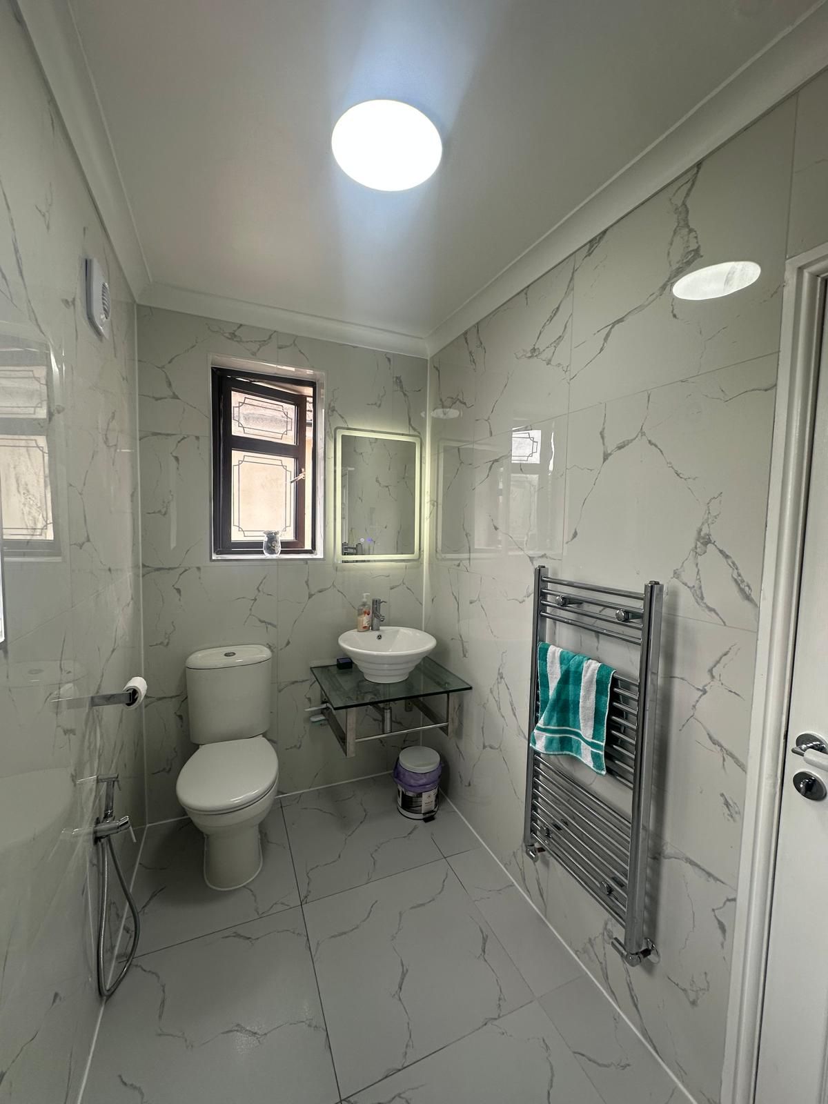 Marble-effect bathroom with a matte black heated towel rail by JFA Construction Group
